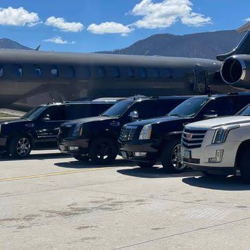 Luxury SUVs lined up beside a private jet with mountains in the distance
